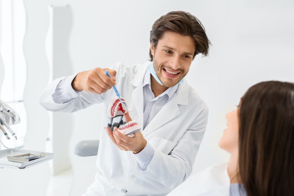 cheerful doctor showing how to brush teeth using jaw model Mason Dentistry New Home